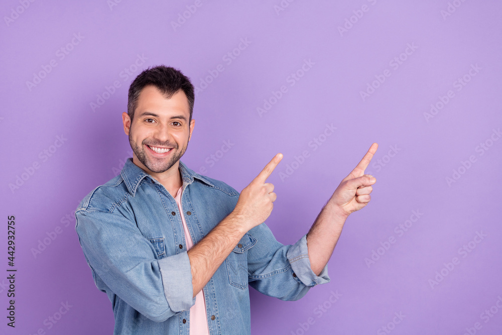 Photo of young man happy positive smile indicate fingers empty space direct way follow advert isolated over violet color background Photo of young man happy positive smile indicate fingers empty space direct way follow advert isolated over violet color background