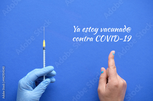 Spanish text Ya estoy vacunado contra COVID means I got my COVID 19 vaccine in English. Vaccination motivator concept. Medic hand in glove with syringe. Hand with index finger pointing at text. photo