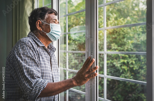 An elderly male patient wearing a mask alone at home and looking out the window.