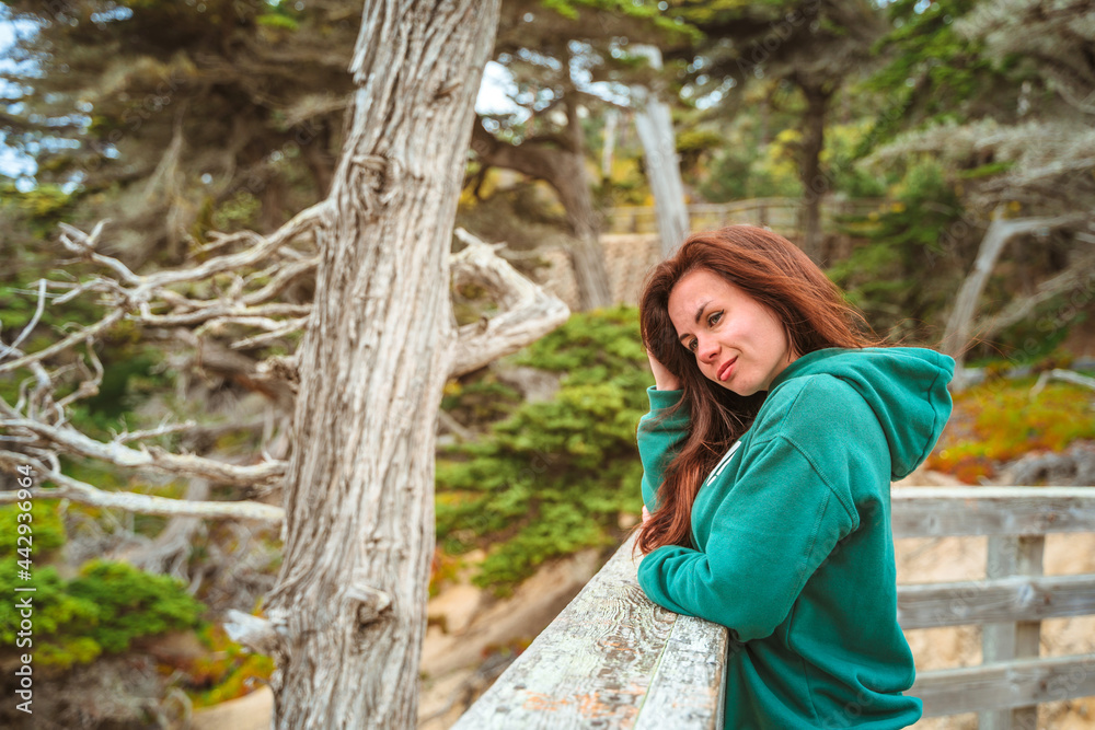 A young woman walks in the park near a lonely cypress tree and admires the ocean in California