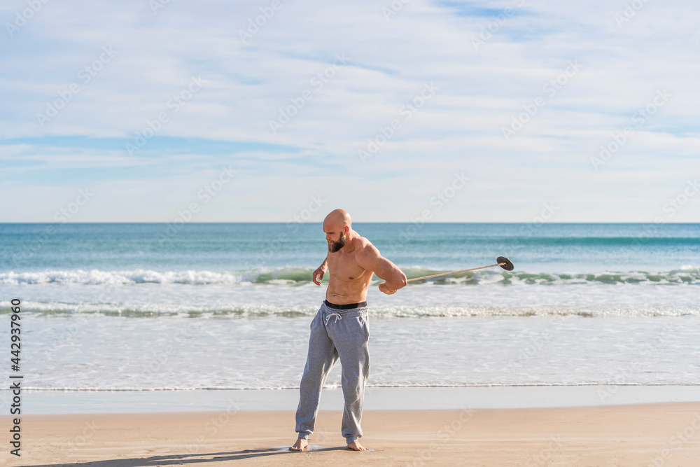 Athlete passing weight around body training on beach Athlete passing weight around body training on beach