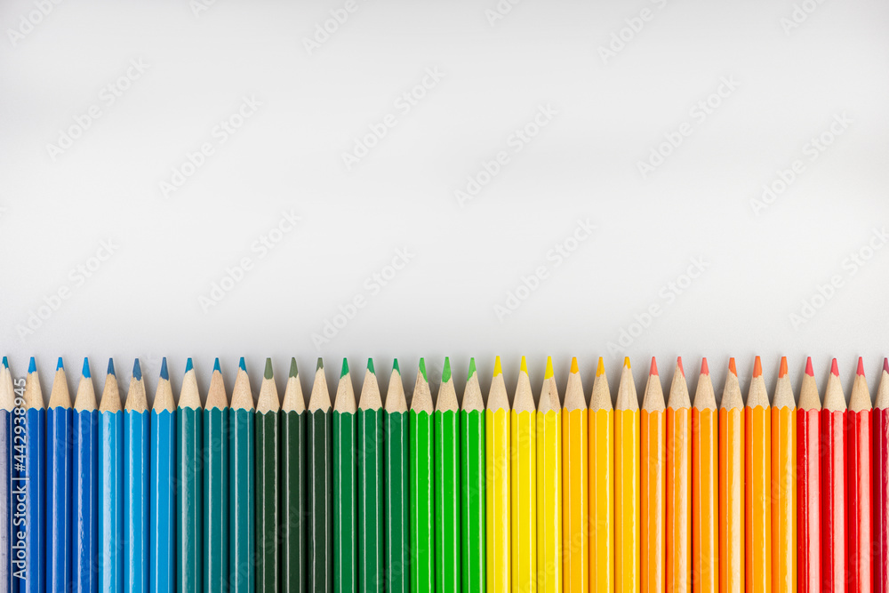 Row of colored pencils on a white sheet of paper. Row of colored pencils on a white sheet of paper.