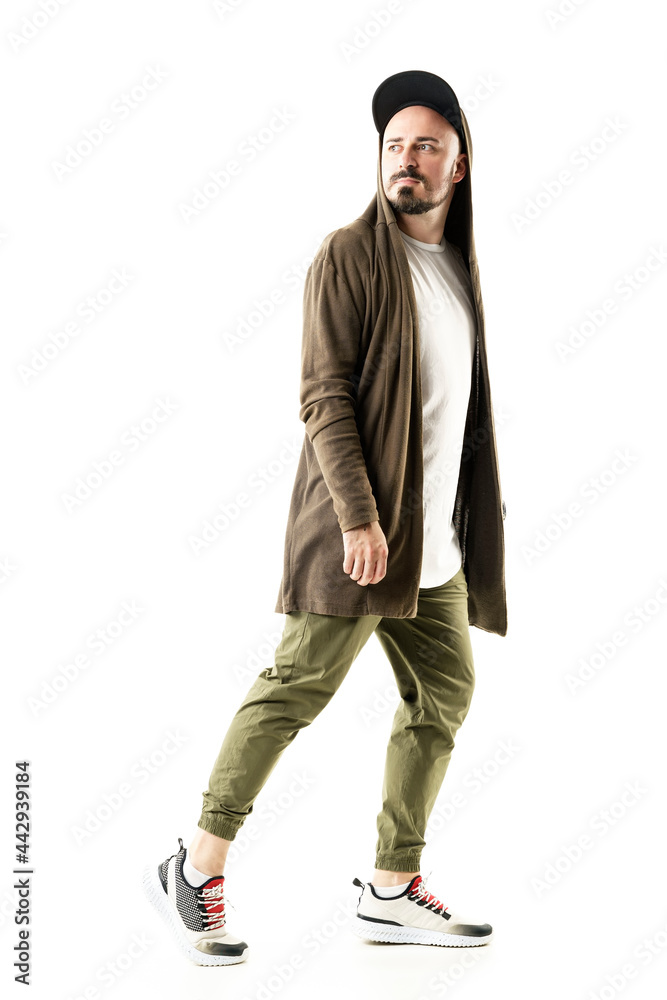 Side view of stylish trendy man with cap and hooded cardigan walking and looking back. Full body portrait isolated on white background