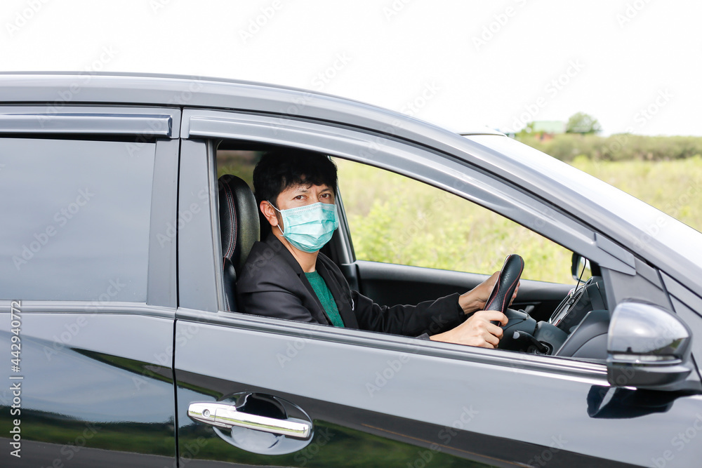 A man wearing a work suit drives a sedan to work in the city. wearing a medical mask to prevent infection during the coronavirus epidemic The driver of the sedan wears a mask for Covid-19.