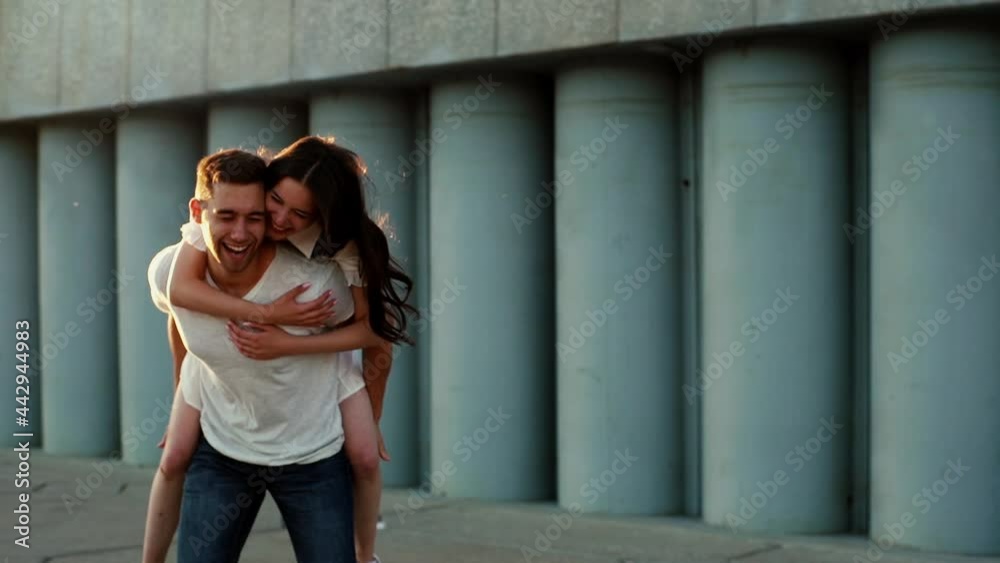 Portrait of young cheerful woman running and jumping on back of boyfriend outdoors. Happy couple in love having romantic dating outside. Caucasian millennial couple enjoying summer time together.