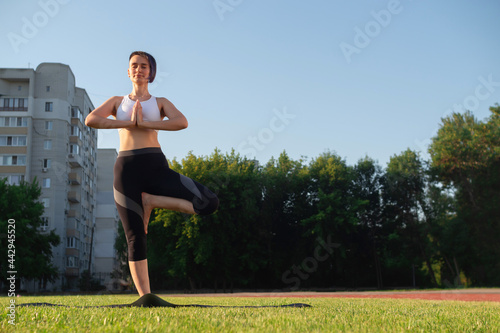 An athletic, fair-skinned young woman of athletic build is practicing yoga in the park. The concept of healthy living, self-care and wellness