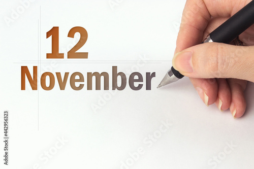 November 12nd. Day 12 of month, Calendar date. The hand holds a black pen and writes the calendar date. Autumn month, day of the year concept. photo