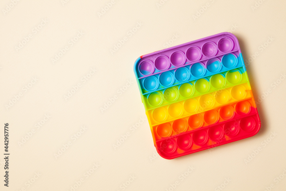 Rainbow silicone sensory antistress pop it toy on light brown background. Top view. Space for text. Rainbow silicone sensory antistress pop it toy on light brown background. Top view. Space for text.