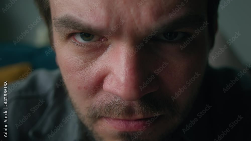Emotional angry man portrait, brutal male person with beard frowning, sitting on sofa in living room, looking in camera. Feeling irritation and anger.