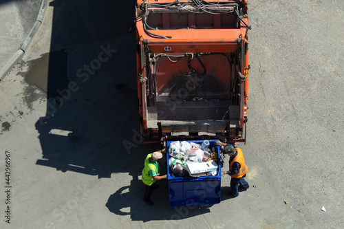 Garbage removal. The scavengers are rolling the trash can to the garbage truck, top view. Garbage loading process.