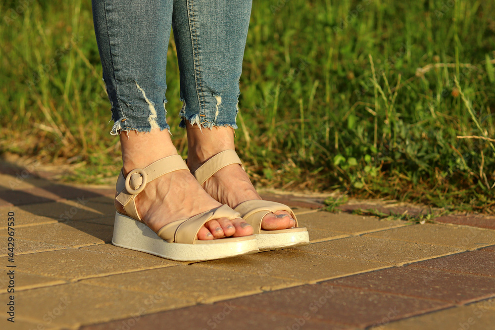 Women's legs in blue jeans and light sandals