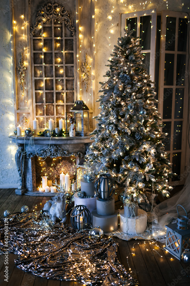 warm and cozy evening in Christmas room interior design,Xmas tree decorated by lights presents gifts,toys, deer,candles, lanterns, garland lighting indoors fireplace.holiday living room.magic New year