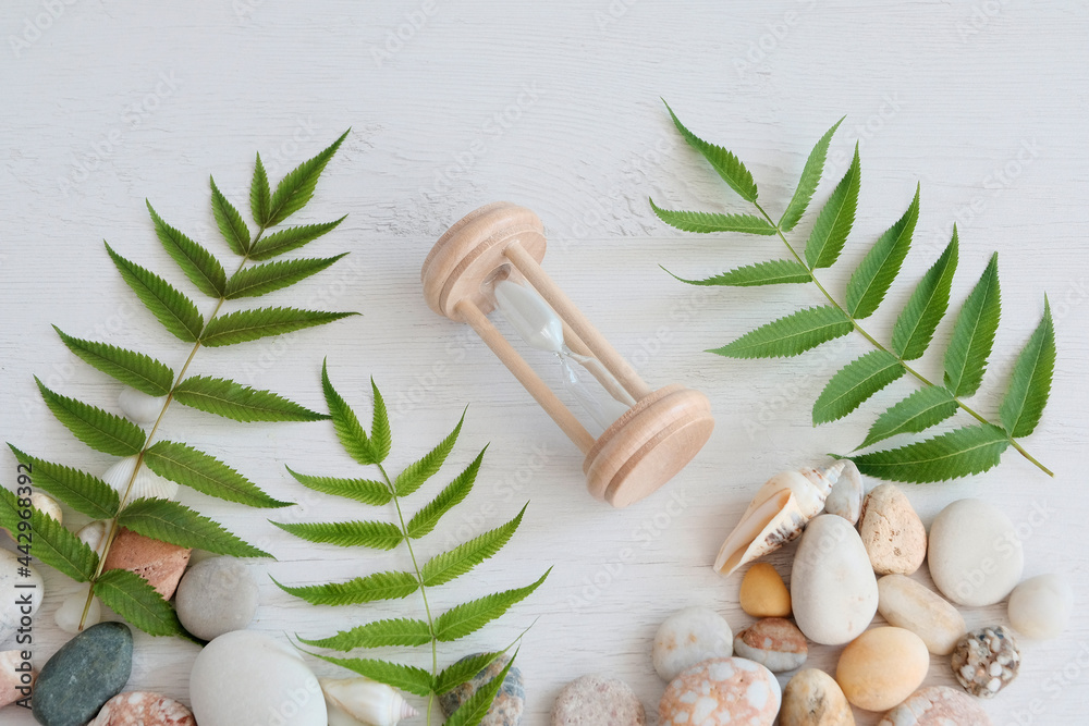 Hourglass in the center next to leaves and sea stones. Background for spa treatments. Relax composition concept