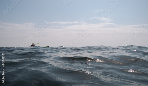 Open sea. Focus on the foreground. A man is sailing on a kayak in the background