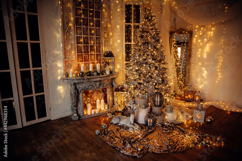 warm and cozy evening in Christmas room interior design,Xmas tree decorated by lights presents gifts,toys, deer,candles, lanterns, garland lighting indoors fireplace.holiday living room.magic New year