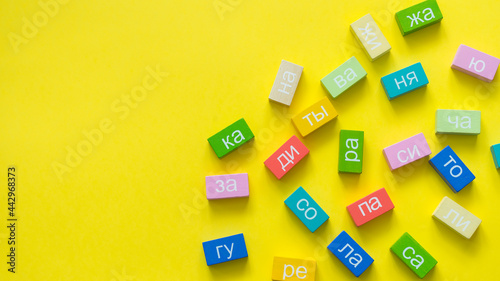 Multicolored cubes from the syllables of the Russian language on a yellow background. The concept of teaching reading © SEA_Ekaterina