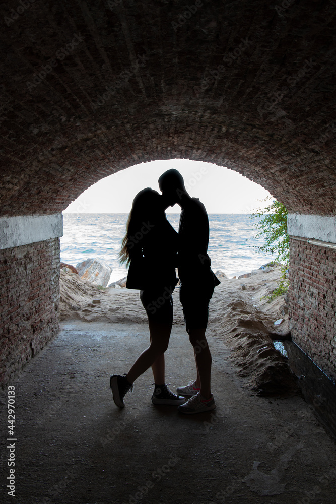 In love man and woman silhouette kissing under a tunnel with the sea in the background.