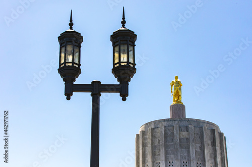 Iconic gleaming golden man statue atop the dome of the Salem, Oregon capitol building with symbolic light post in foreground with bright blue sky on a sunny afternoon. photo