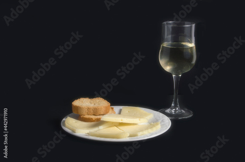 still life with plate with cheese and bread and a glass of white wine, isolated on black background