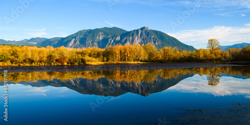 Fall colors reflect in the calm water of Borst Lake also known as Snoqualmie Mill Pond from its role in the former lumber yard. Mount Si rises on a sunny blue sky day