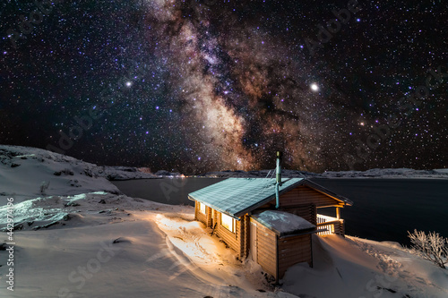 Fototapeta Naklejka Na Ścianę i Meble -  Wooden cottage by the lake in winter. Night sky, Milky Way. Winter holidays.