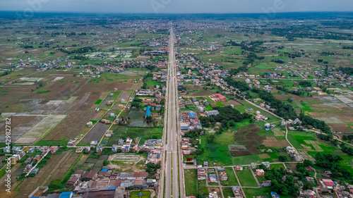 Aerial view of six-lane highway passing through meadows, fields and scattered houses towards mountains in countryside Nepal. photo