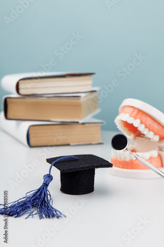Model of jaw with dentist tool and graduation cap with books. Medical education concept. Vertical image