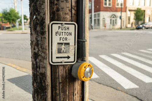 an old, beat up crosswalk icon sign with arrow that reads, push button to cross, above electronic signal switch for pedestrians to press photo