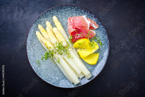Traditional steamed white asparagus with cured ham and boiled potatoes garnished with butter sauce served as top view on a Nordic design plate with copy space