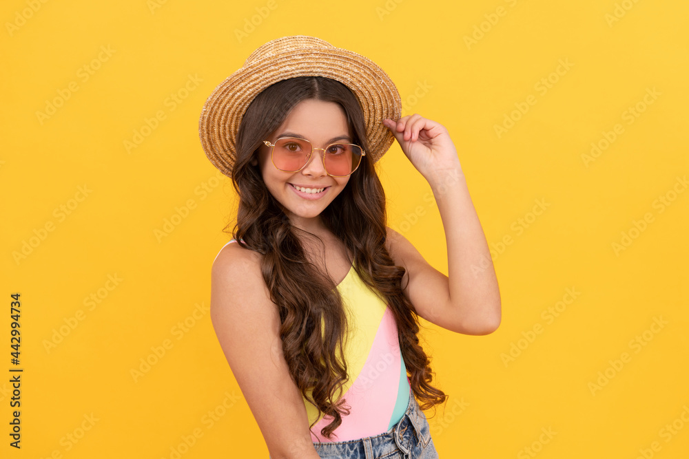 happy teen girl in summer straw hat and glasses has curly hair on yellow background, happiness