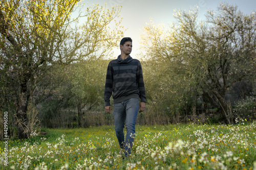 Young man  in field of wild flowers. Behind him, the falling sun illuminates the scene © magui RF