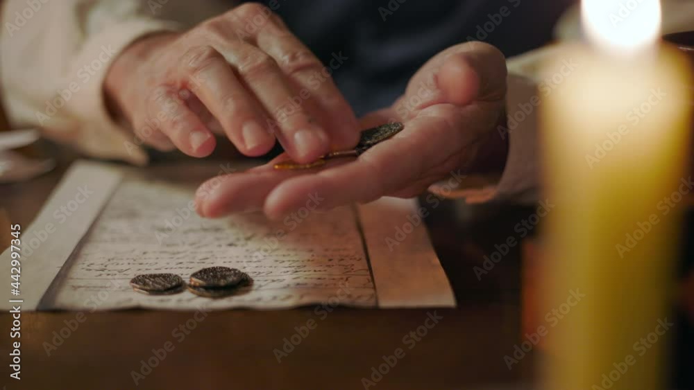 A close up candlelit scene of a Caucasian 18th century man counting and sorting various types of coins from his coin collection. A close up candlelit scene of a Caucasian 18th century man counting and sorting various types of coins from his coin collection.