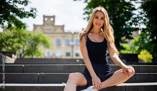 Young blonde sportive woman in a black tank top and in black tight sports shorts sits on the stairs