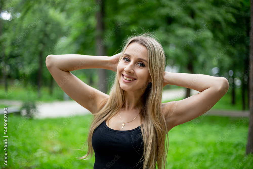 Young beautiful sporty blonde woman in a black T-shirt and in black tight sports shorts in good shape posing in front of green trees Young beautiful sporty blonde woman in a black T-shirt and in black tight sports shorts in good shape posing in front of green trees
