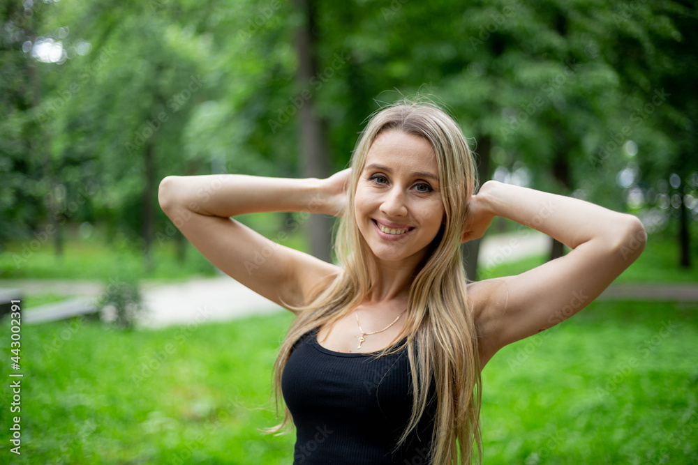 Young beautiful sporty blonde woman in a black T-shirt and in black tight sports shorts in good shape posing in front of green trees Young beautiful sporty blonde woman in a black T-shirt and in black tight sports shorts in good shape posing in front of green trees