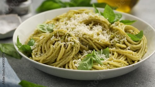 Basil pesto spaghetti pasta in a white bowl with parmesan, camera slides while parmesan is grated on top