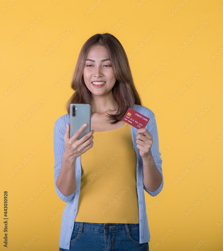 Excited Asian woman holding credit card and smartphone feeling excited while looking at mobile phone isolated on colour background Excited Asian woman holding credit card and smartphone feeling excited while looking at mobile phone isolated on colour background