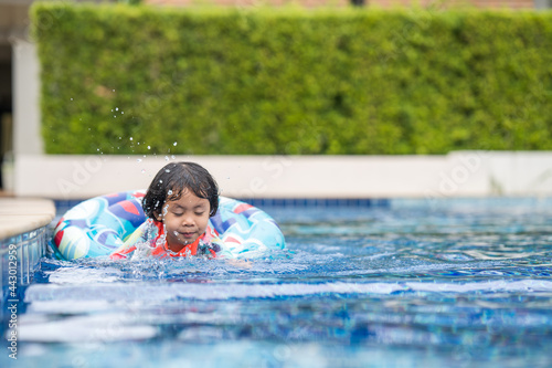 Little Adorable girl with Inflatable Pool Float have fun at outdoor swimming pool in summer.