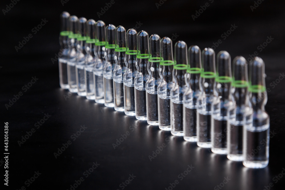 Small glass injection bottles with medicine on a black background. Small glass injection bottles with medicine on a black background.