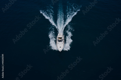 Fototapeta Naklejka Na Ścianę i Meble -  Large white yacht on the water in motion top view. Luxury motor boat on dark blue water aerial view. The yacht is fast moving on dark water. Travel on high-speed boats on the water.