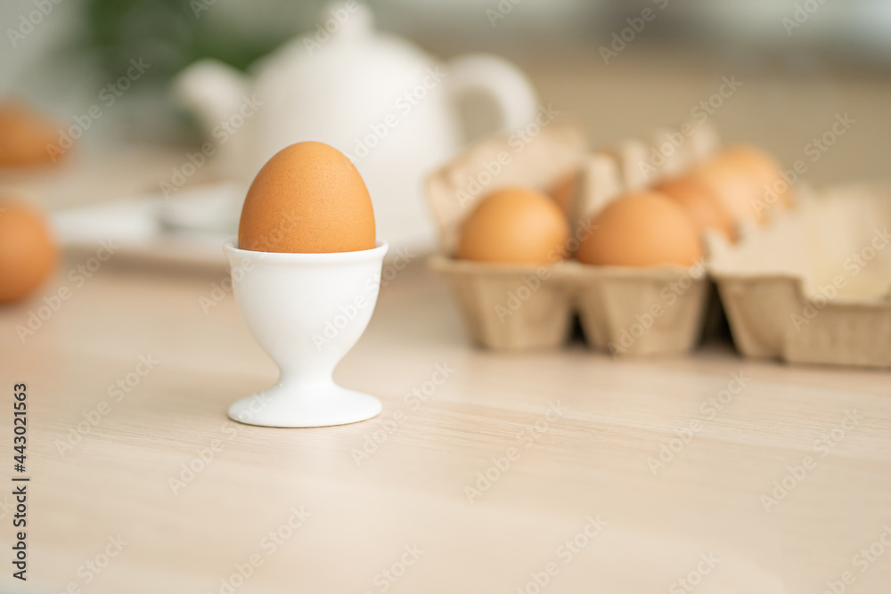 Selective focus at one boiled egg put on the kitchen desk with blurred eggs carton background of kitchen equipment ready to prepare food meal for breakfast. With copy space for add text Selective focus at one boiled egg put on the kitchen desk with blurred eggs carton background of kitchen equipment ready to prepare food meal for breakfast. With copy space for add text