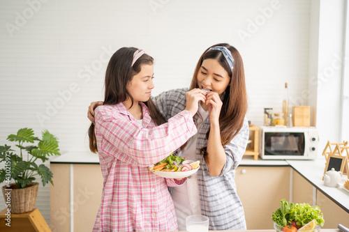 Mixed race girl younger and older sister talk and smile while play with each other inside of the kitchen in the morning while ear breakfast. Family relationship, bond, love and togetherness concept. photo