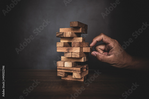 Close-up hand is placing wood block stack in tower shape with caution to prevent collapse or crash concepts of financial risk management and strategic planning.