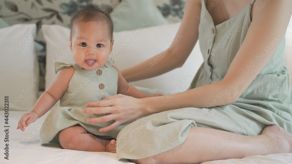Obraz premium asian woman mother parent encourage baby infant to sit and crawl on soft bed at luxury home. 6 months kid put effort learning lesson development skill. mom playing with baby infant on bed in bedroom.