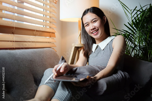 Smiling young woman sitting on comfortable sofa and using digital tablet. 