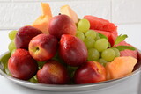 Fruit mix. Nectarine, grapes,  watermelon, melon. Pieces of fruit on a plate lie on a silver tray on white background.