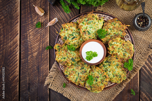Zucchini fritters. Vegetable vegetarian zucchini pancakes with sauce on wooden background. Healthy food. Top view, flat lay