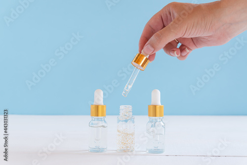 female hand with Dropper of essential oil, aromatherapy essence, beuty serum or medicinal liquid on blue background. Unbranded bottles for your design.