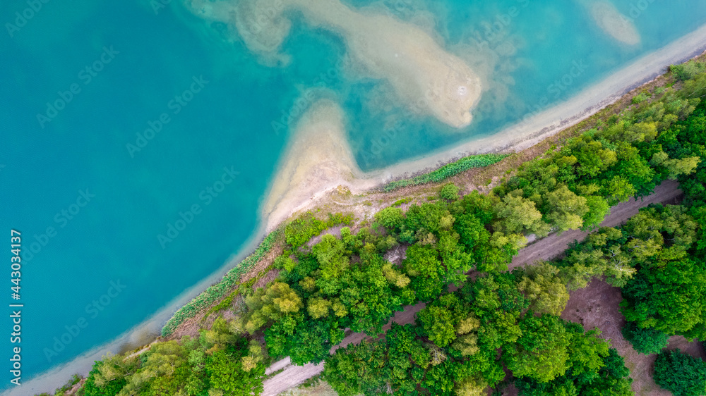 Aerial view of a picturesque place where transparent turquoise water of a forest lake meets a stony shore with trees in spring. captured with a drone. High quality photo
