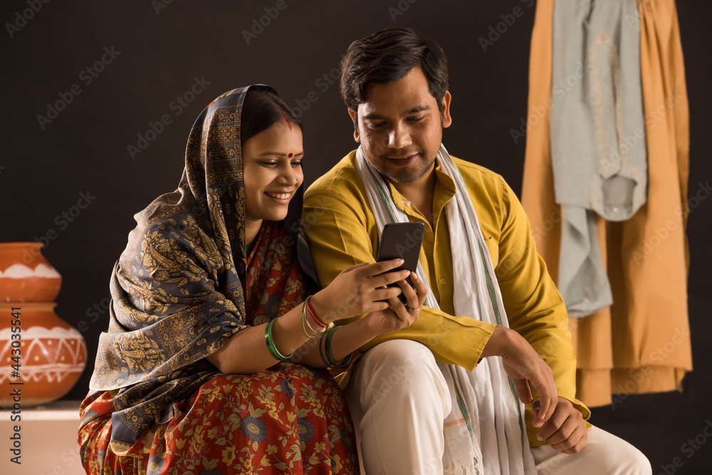 A RURAL WIFE AND HUSBAND SITTING TOGETHER AND USING MOBILE PHONE - obrazy, fototapety, plakaty 
